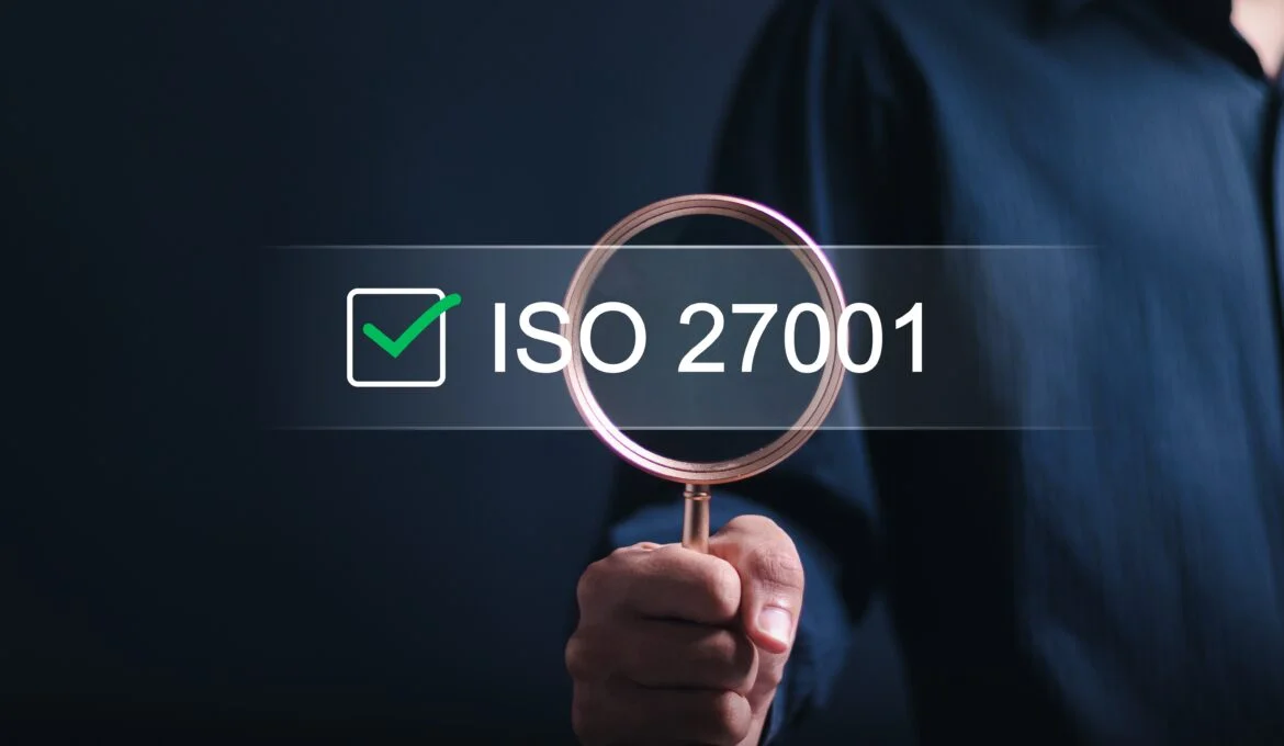 Person holding magnifying glass over the words ISO 27001 certification for Information Security.